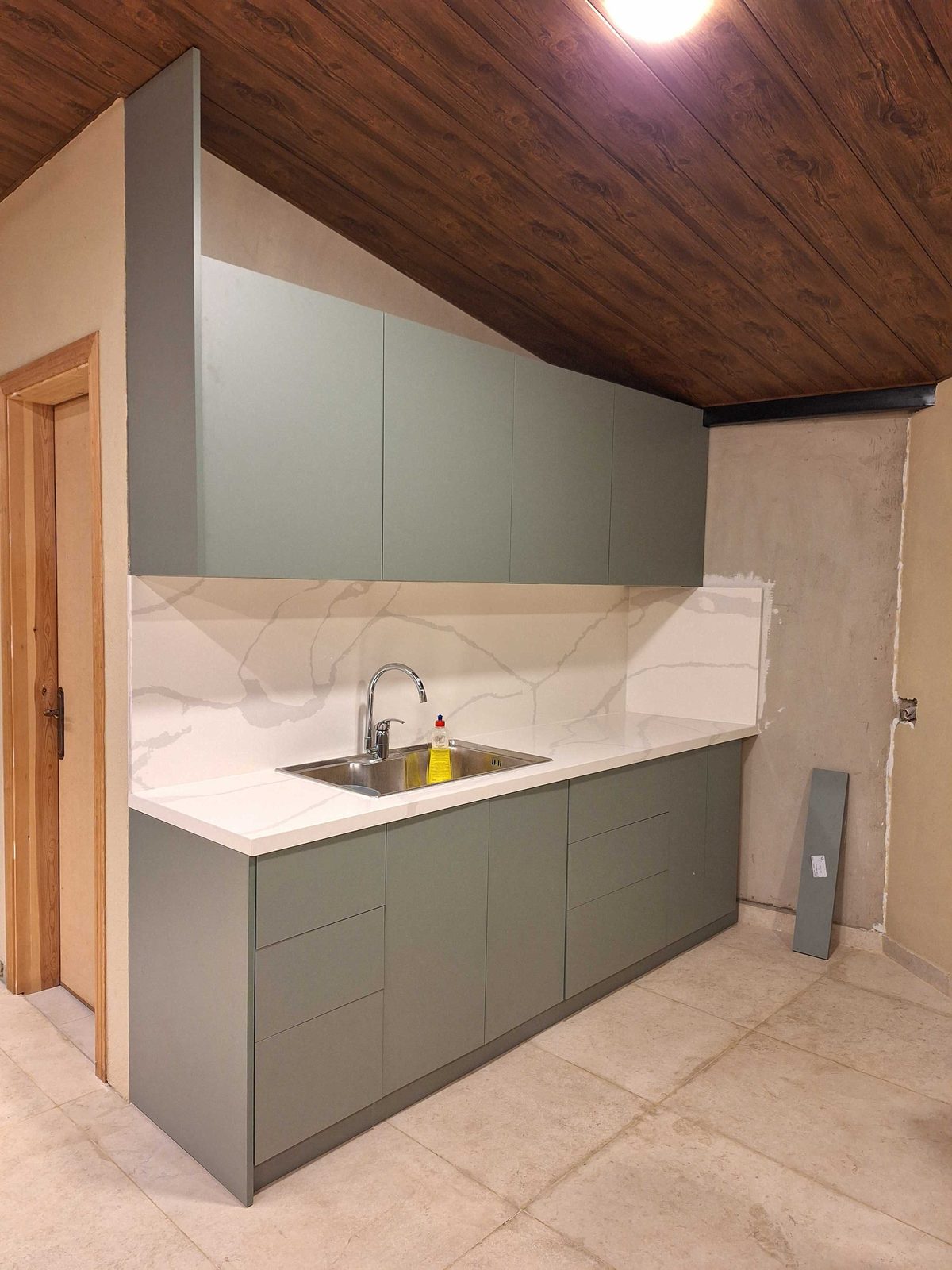 Laurel Green kitchen viewed from the side beneath a sloped wood ceiling